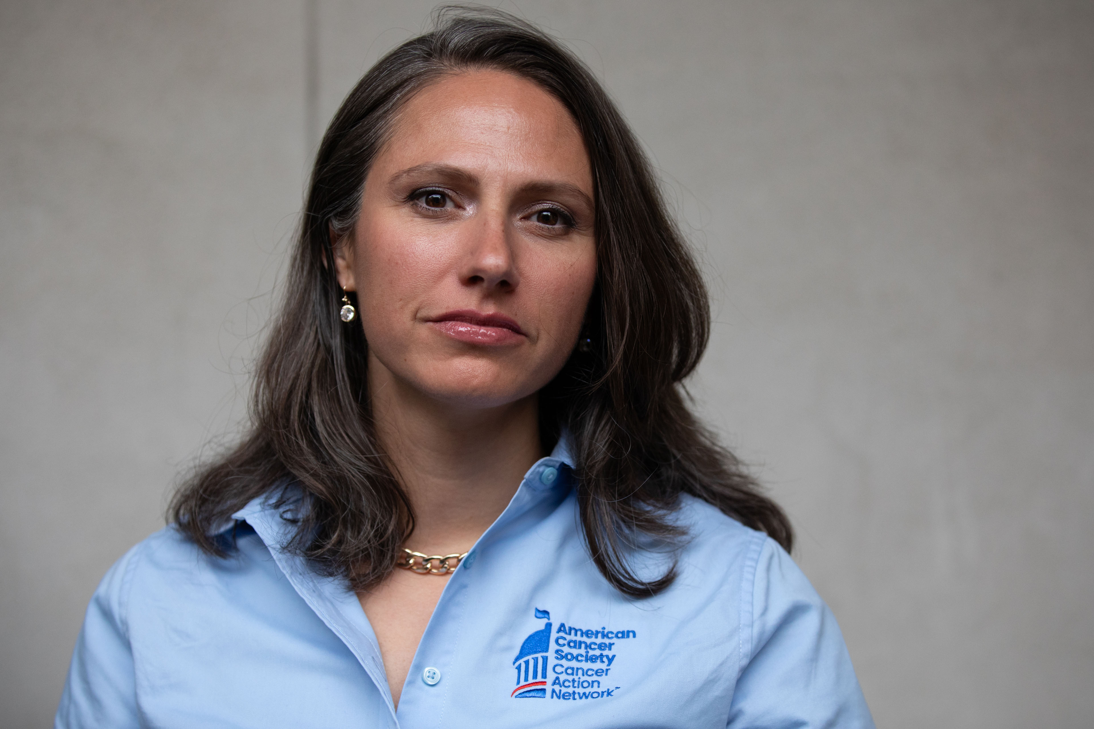 A portrait of a woman wearing a blue shirt standing against a gray background.