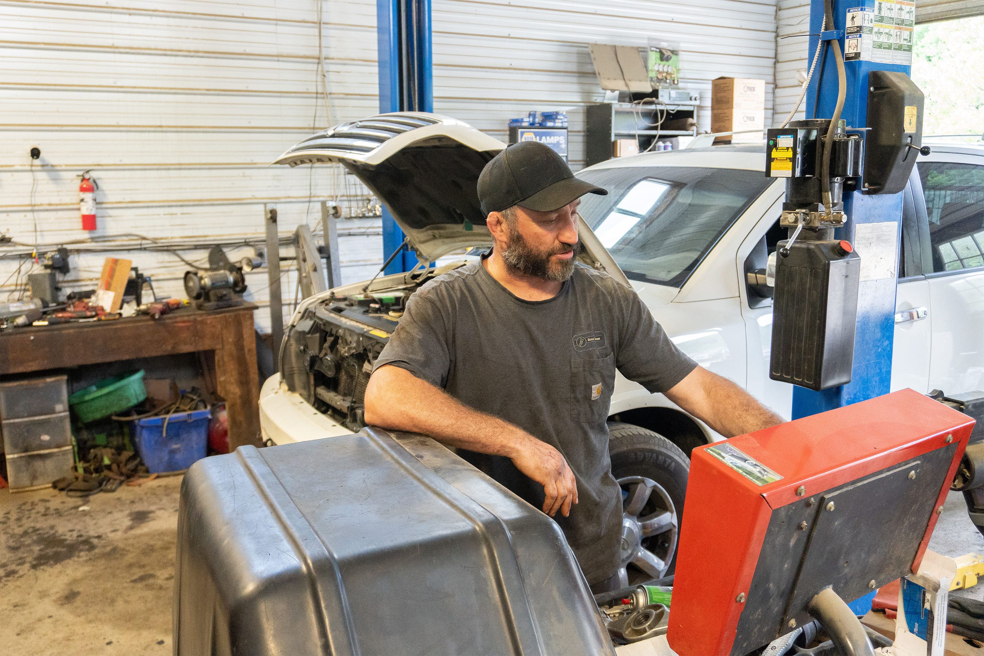 Ross Tobiassen looks at supplies in his mechanic garage. A white SUV is parked behind him with its front hood popped open.
