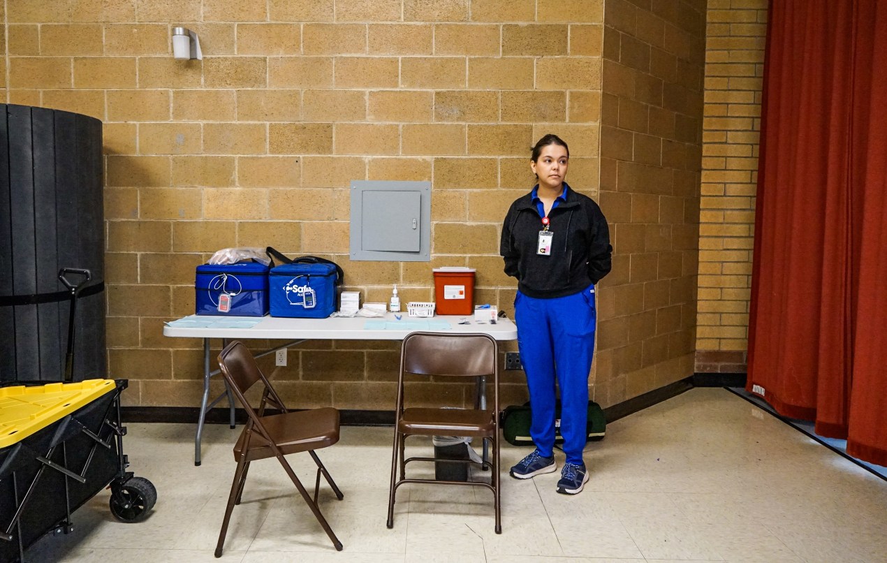 A photo of a nurse standing by a folding table inside of a school.