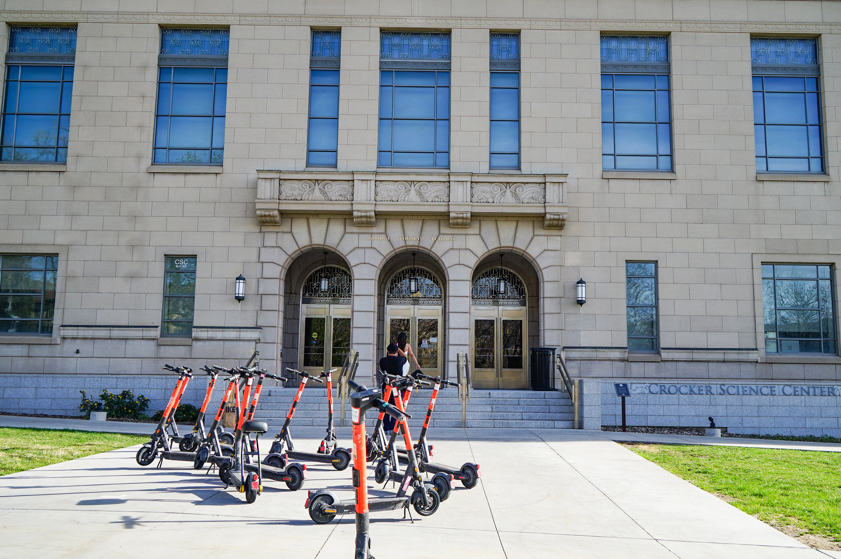 A photo of a university building with several electric scooters parked in front of it.