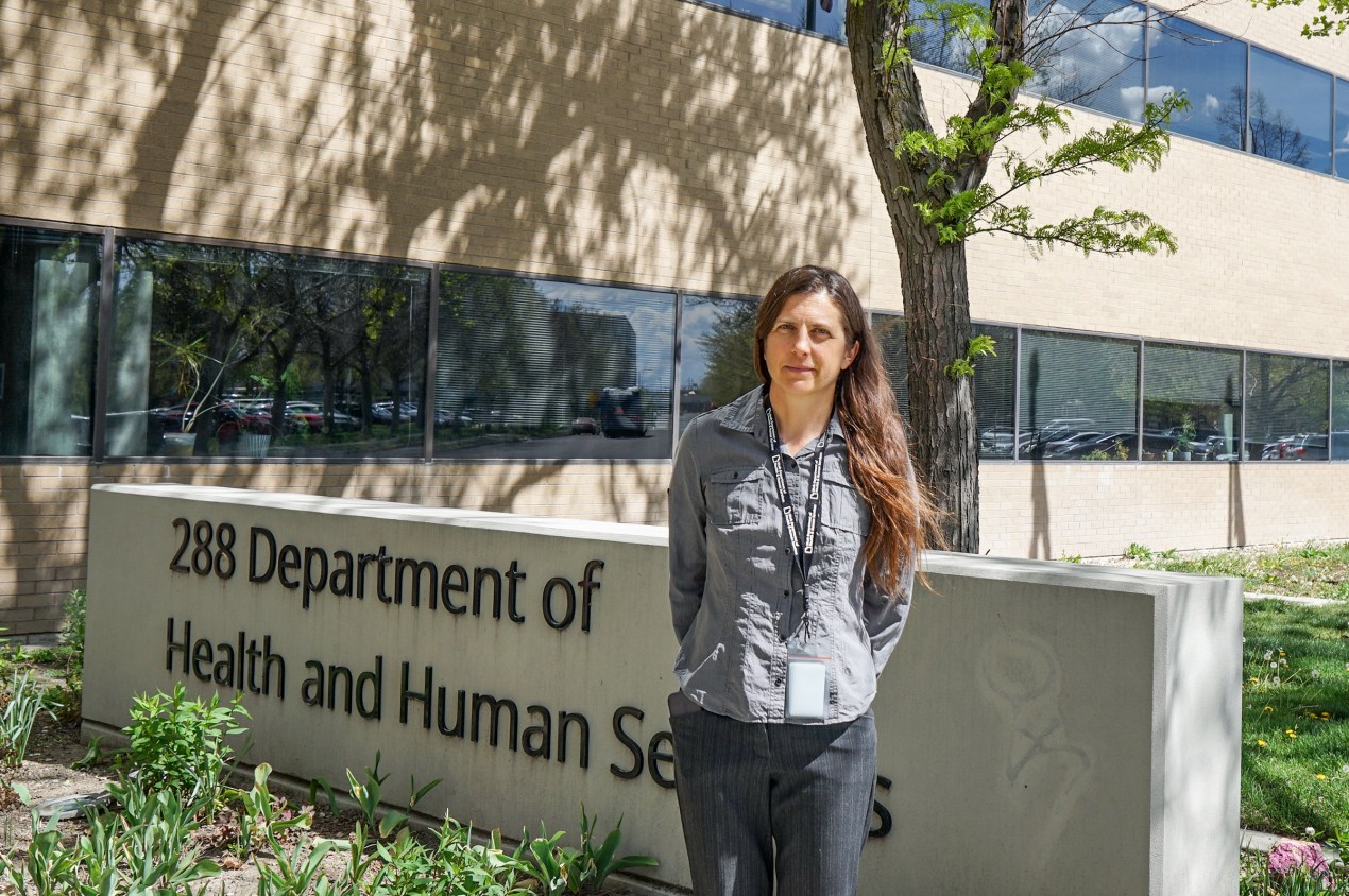 A woman stands outside a building. A sign next to her reads, "288 Department of Health and Human Services."