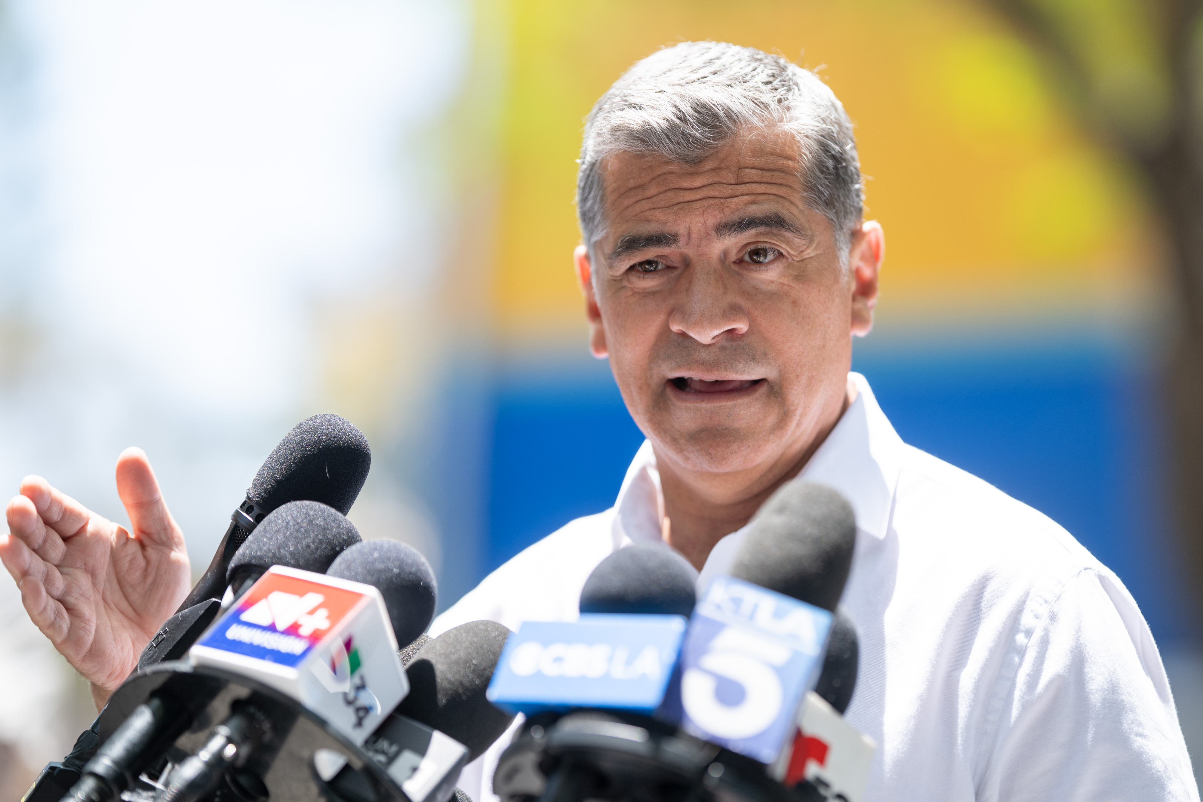 A photo of former HHS Secretary Xavier Becerra speaking in front of news reporters' microphones.