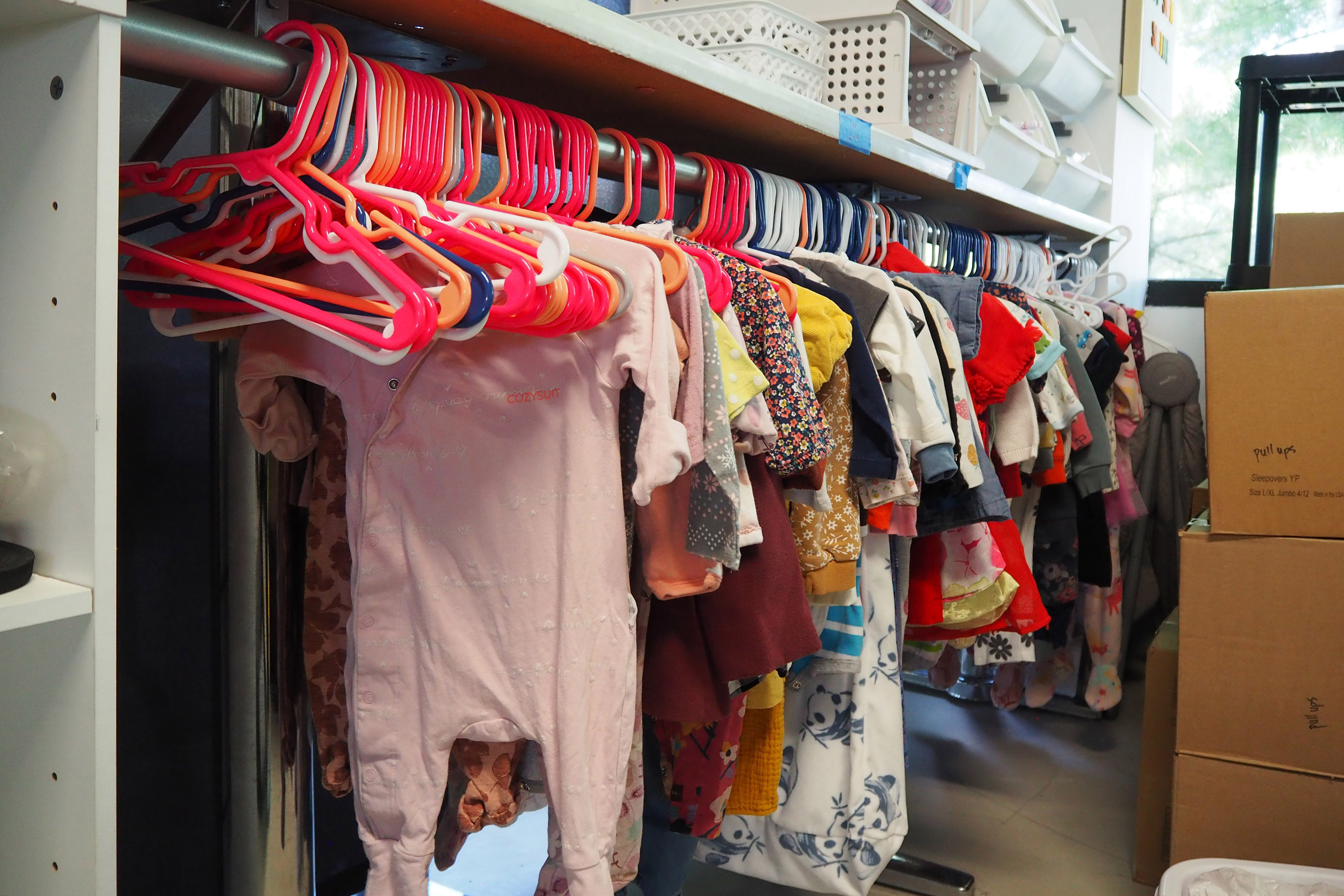 Baby clothing hangs on multicolored hangers on a clothing rack